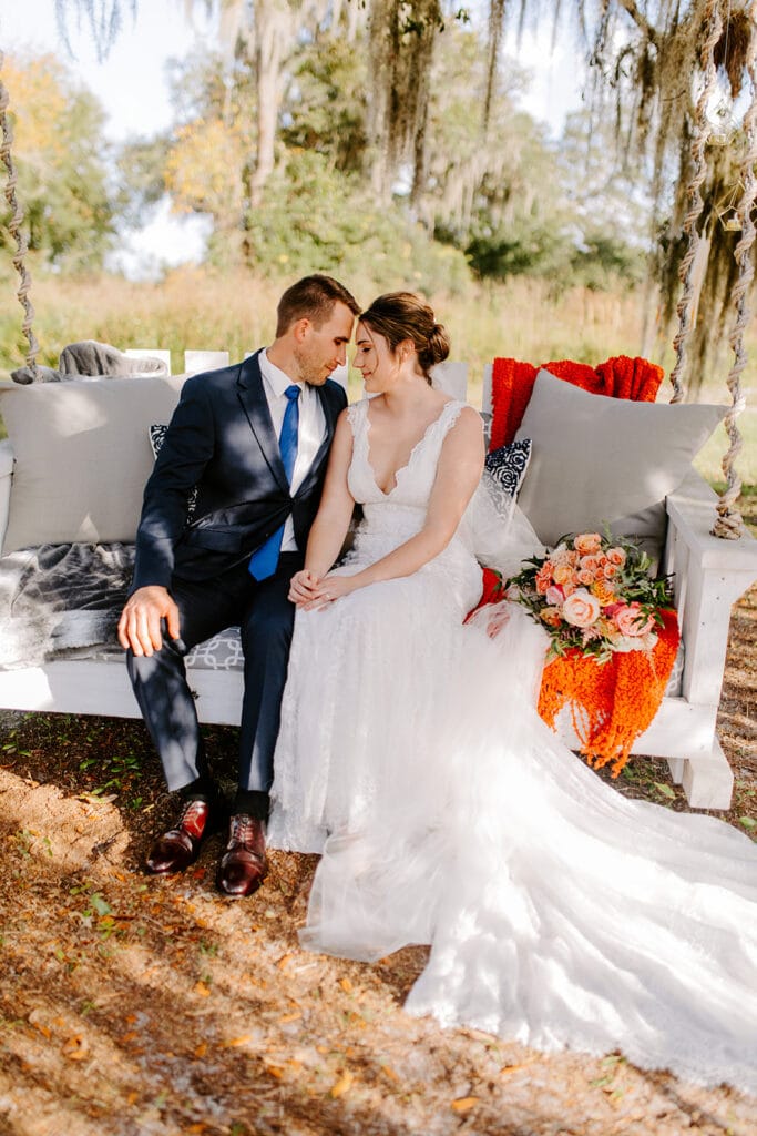 bride and groom on couch with orange flowers under oak tree